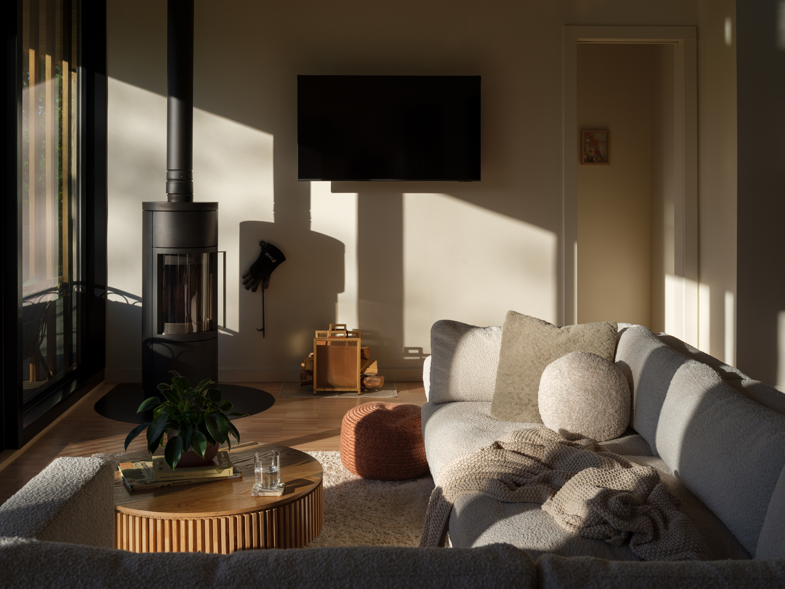 Living room at Será at Sandy Ridge with wood stove, seating, and strong daylight through the forest-facing glazing